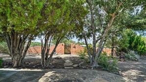 A courtyard with stone pathways, trees, and a rustic building with a gate.