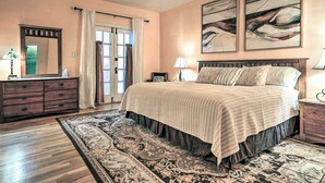 A bedroom with a large bed, a dresser, a mirror, and two wall-mounted paintings.