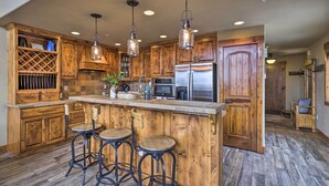 A kitchen with wooden cabinets, a stainless steel refrigerator, and a bar area with stools. - Colorado Lodge w/ Mtn Views - 3 Mi to Winter Park! (Winter Park)