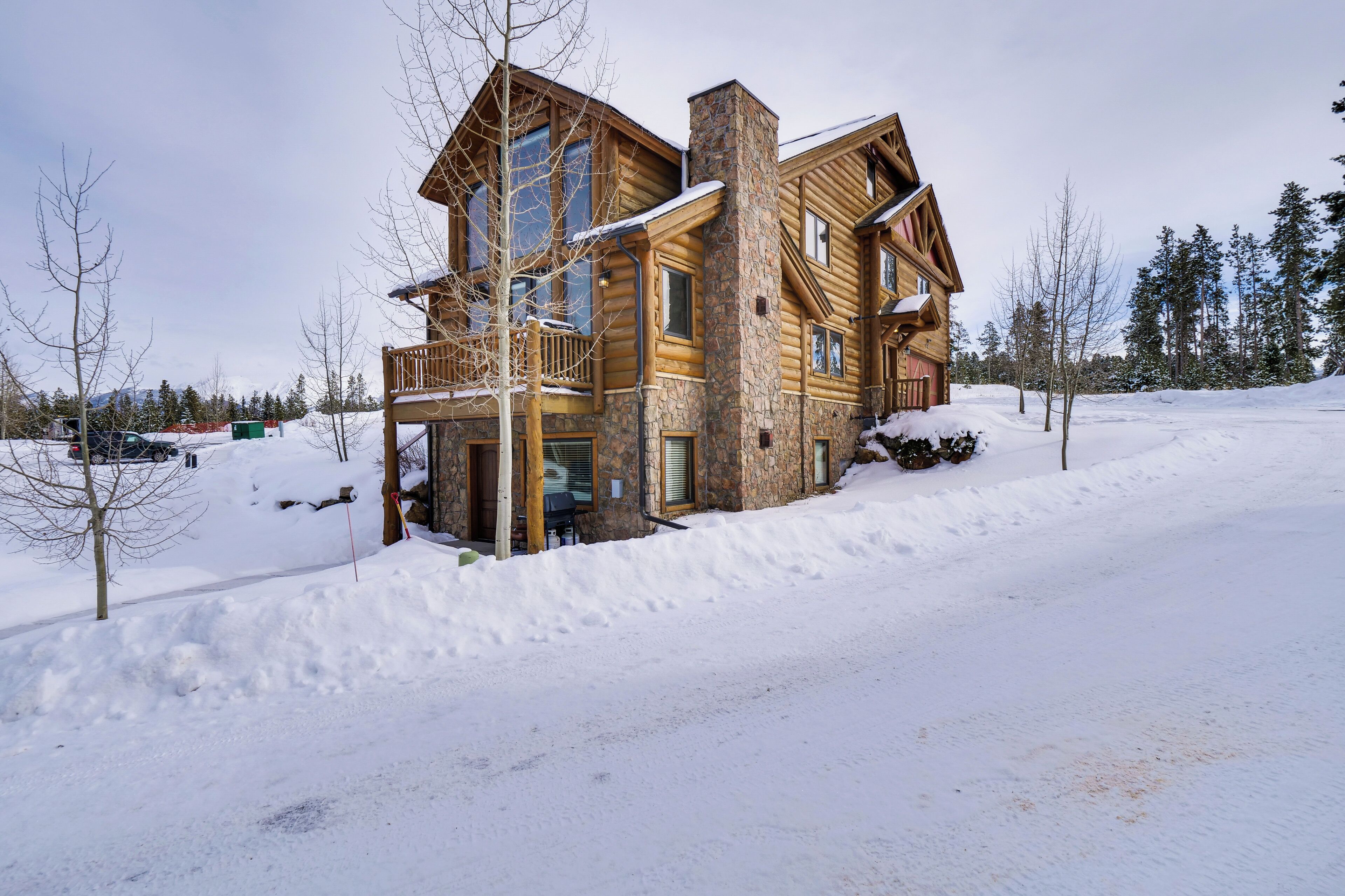 Une grande cabane en rondins à plusieurs niveaux, dotée d’une cheminée en pierre et d’un balcon.