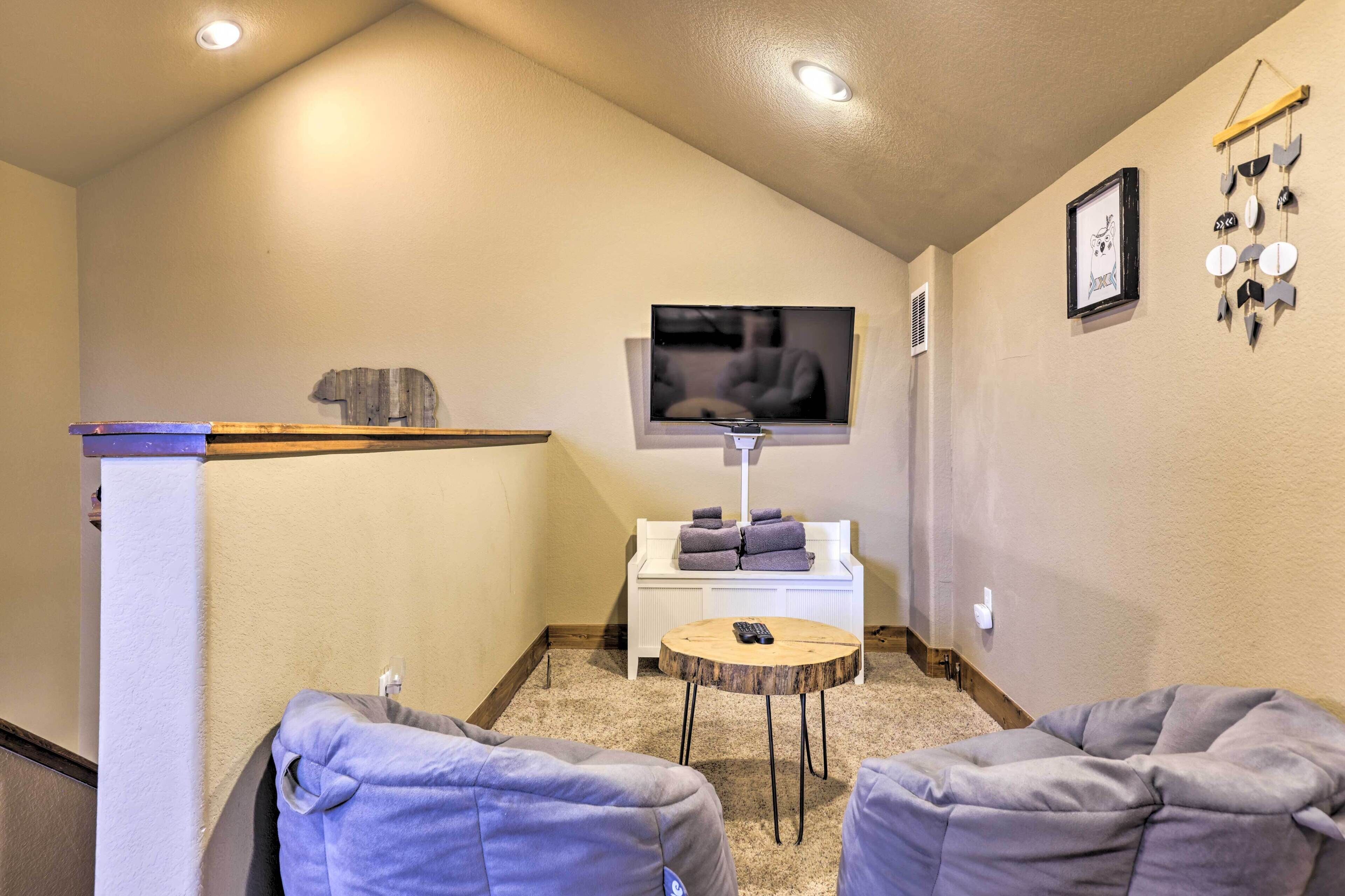 Una sala de estar acogedora con una televisión de pantalla plana, una mesita blanca y dos sillones orejeros grises.