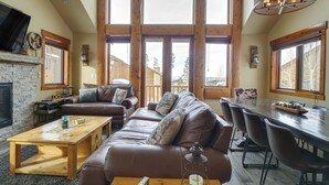 A spacious living area with a large brown leather sofa, a wooden coffee table, and a dining table with chairs. There is a fireplace, a television mounted on the wall, and large windows allowing natural light. - Colorado Lodge w/ Mtn Views - 3 Mi to Winter Park! (Winter Park)