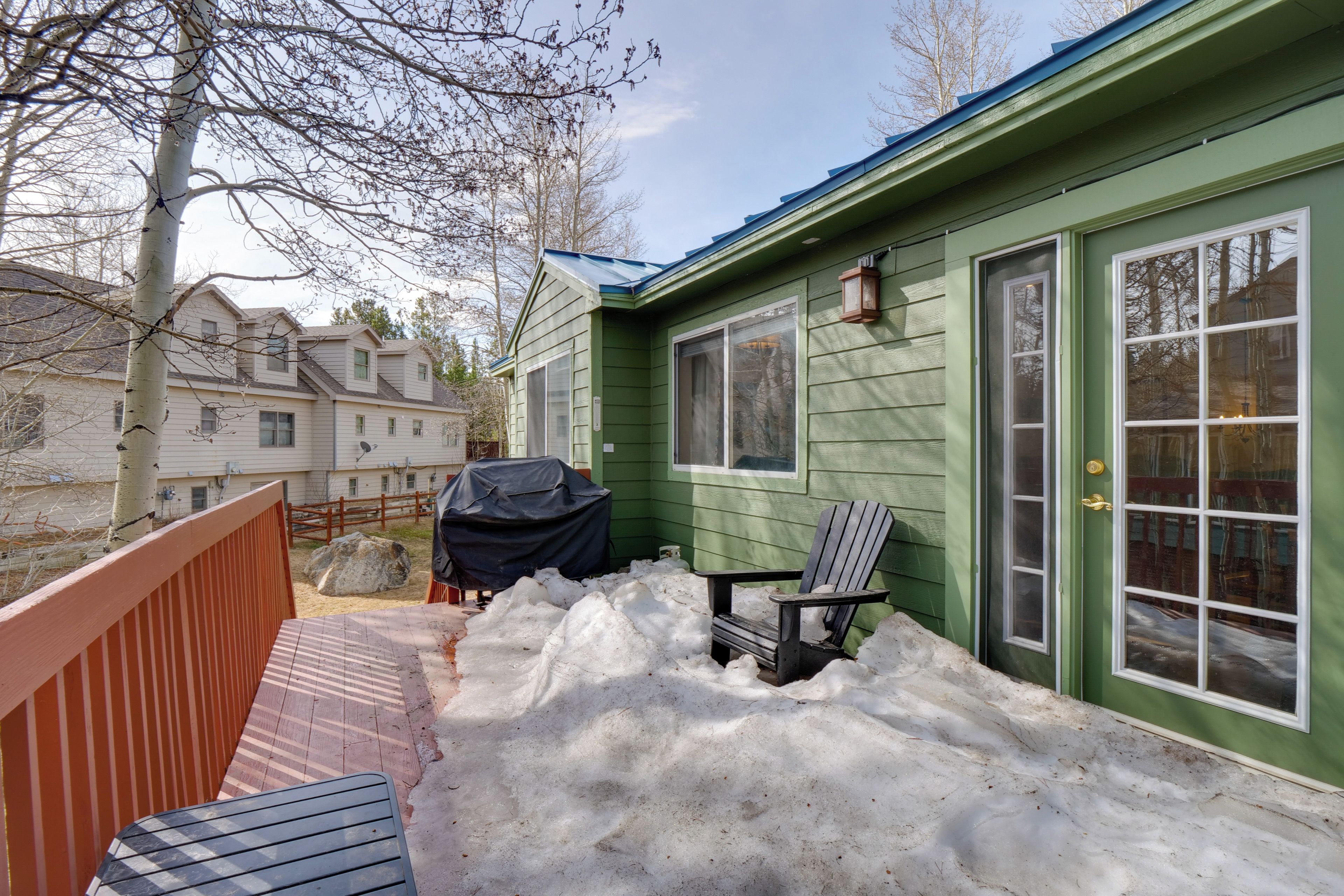 A green house with a covered grill, a wooden deck, and a chair.