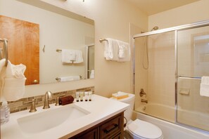 Een badkamer met een wastafel, spiegel, handdoekhouder en een douche met glazen wanden.