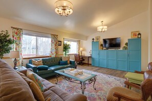 Een woonkamer met een bank, salontafel en een televisie. Er is een bureau met een stoel en een kast.