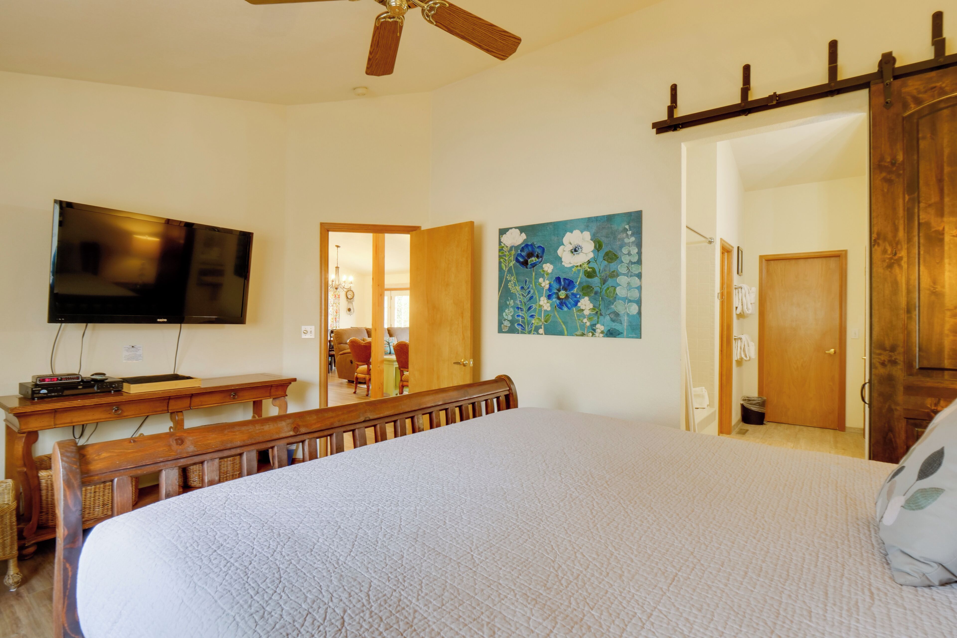 A bedroom with a large bed, a flat-screen TV mounted on the wall, a wooden bench, and a painting.