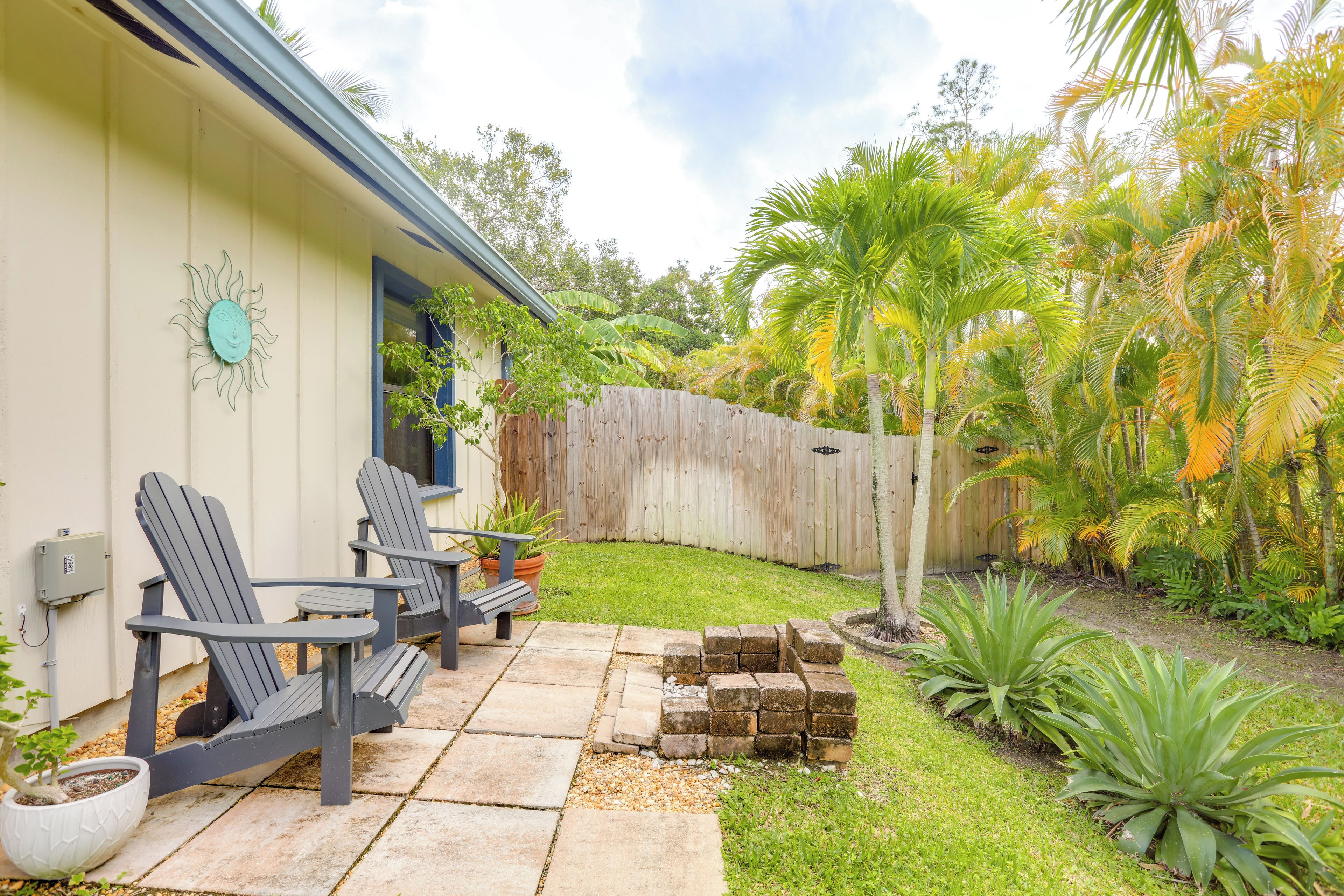 A patio with Adirondack chairs, a wooden fence, and tropical plants.
