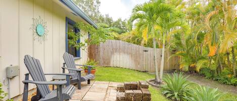 A patio with Adirondack chairs, a wooden fence, and tropical plants.