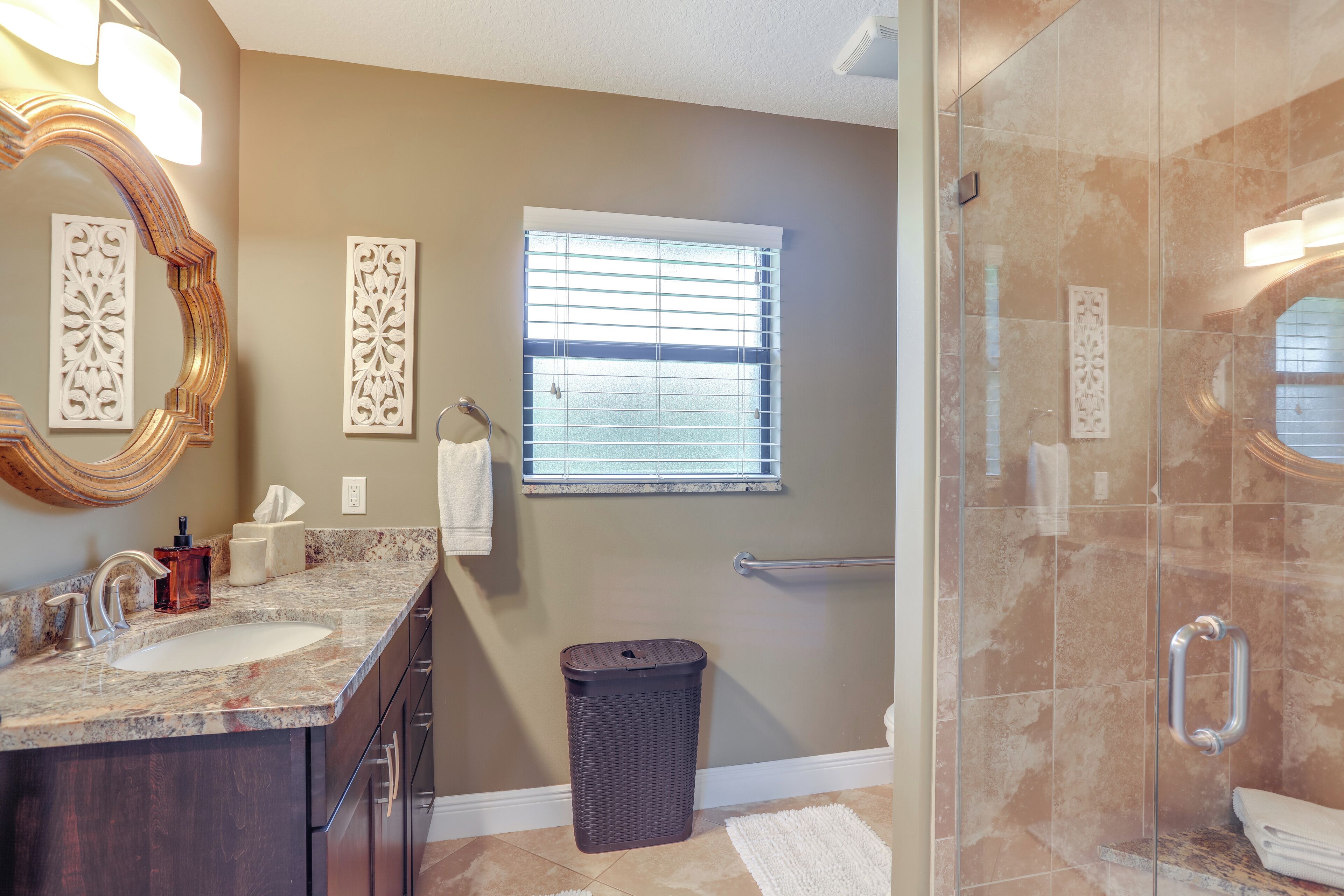 A bathroom with two sinks, a mirror, a window, a trash can, and a shower area.
