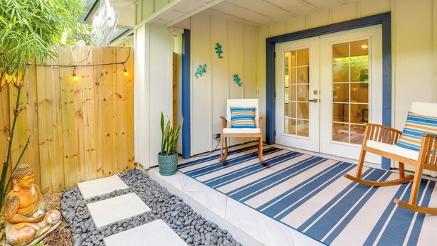 Eine überdachte Veranda mit einem blau gestreiften Teppich, zwei Schaukelstühlen und einer kleinen Buddha-Statue.