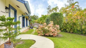 Ein Haus mit einer geschwungenen Auffahrt, einem kleinen Garten mit einer Palme und einem Busch, und einem Holzzaun im Hintergrund.