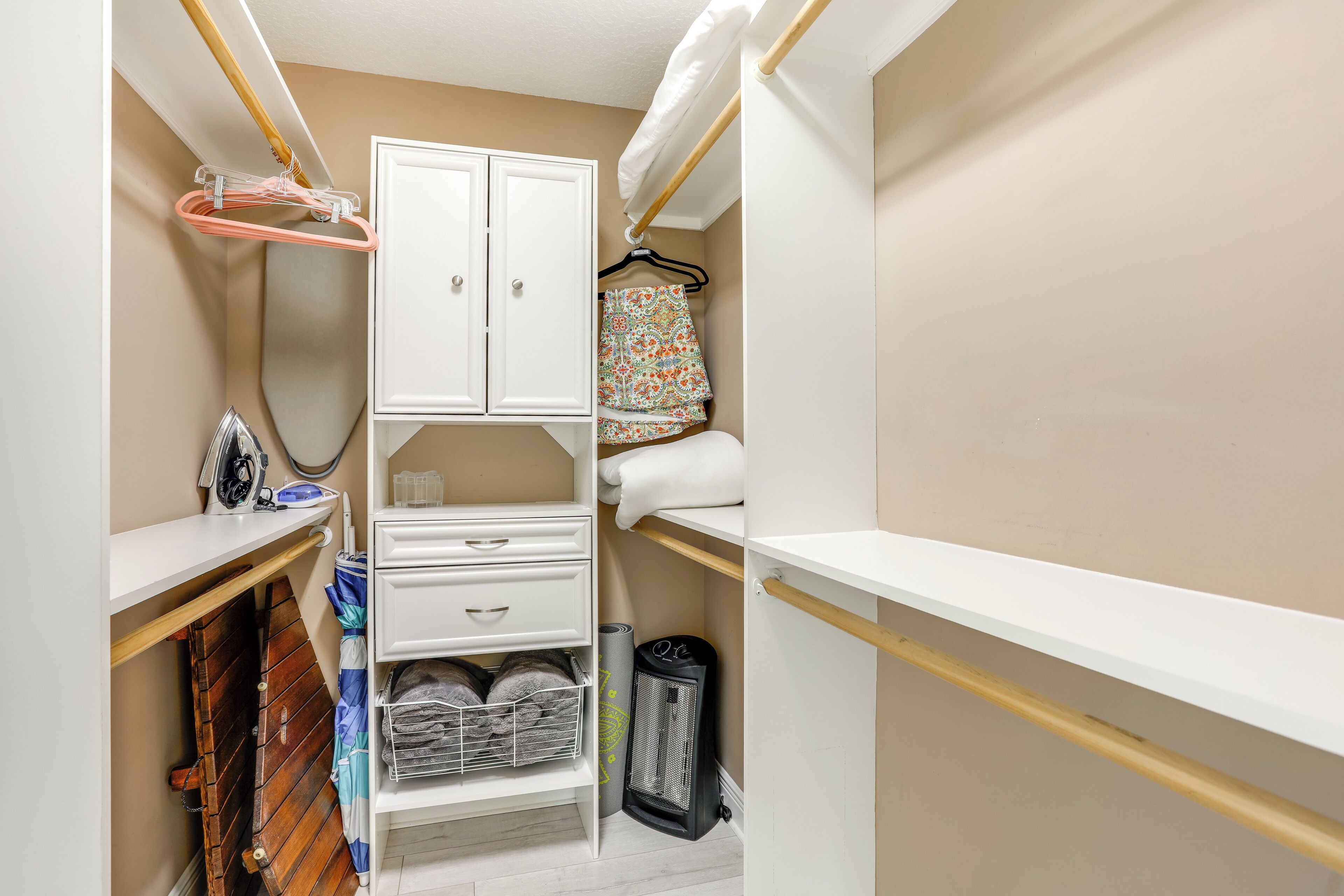 A compact, well-organized closet with white cabinetry, a hanging rack, and shelves for storage.