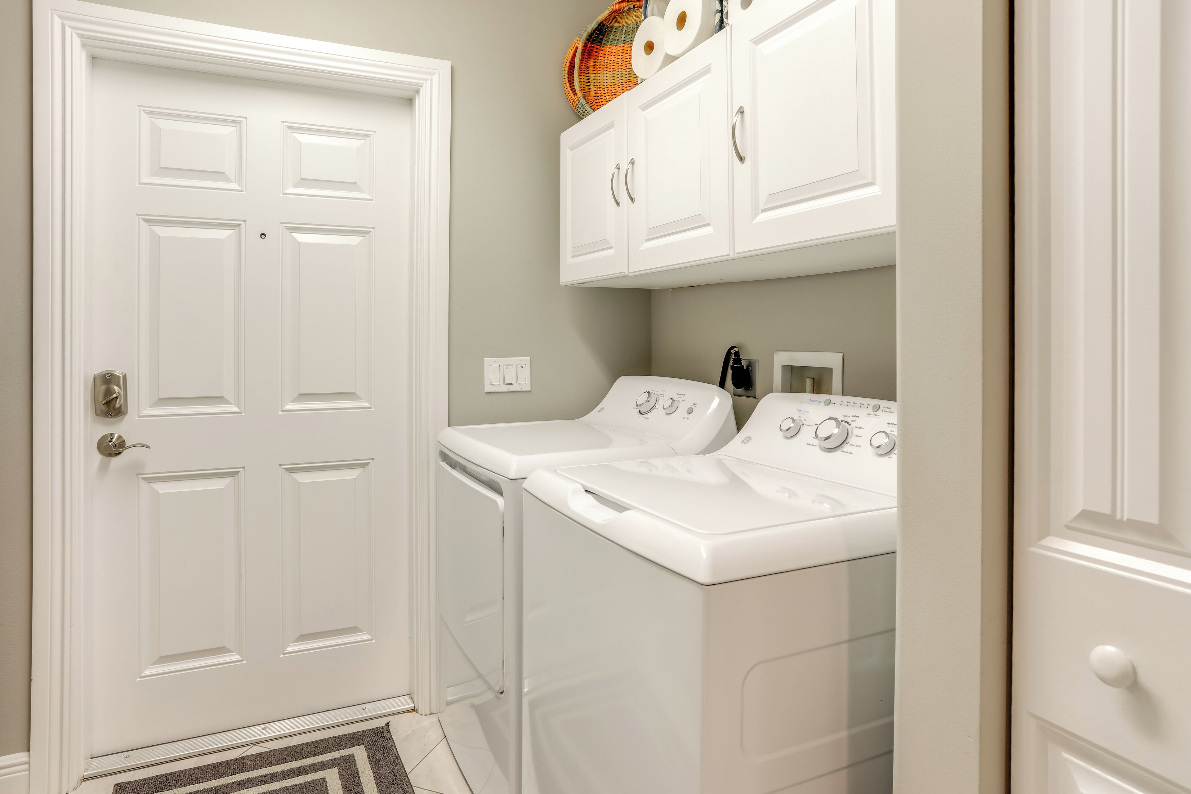 A laundry room with two white front-loading washers and dryers, a white door, and a cabinet above the dryers.