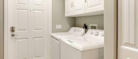 A laundry room with two white front-loading washers and dryers, a white door, and a cabinet above the dryers.