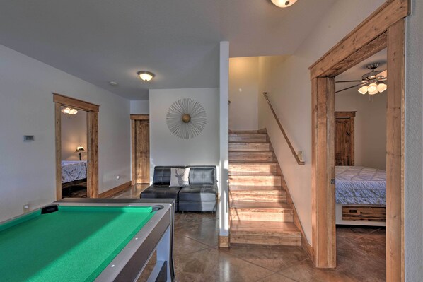 A pool table in a room with a wooden staircase, a sofa, and a decorative wall piece.