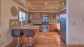 A modern kitchen with wooden cabinets, stainless steel appliances, and a central island with bar stools. - Fairplay Cabin w/ Pool Table, Deck & Mountain View (Fairplay)