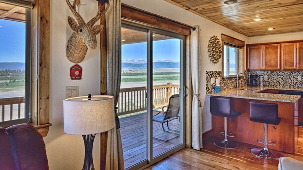 A spacious room with a large sliding glass door leading to a balcony, a kitchen area with wooden cabinets, and a bar with stools. - Fairplay Cabin w/ Pool Table, Deck & Mountain View (Fairplay)