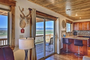 A room with a large sliding glass door leading to a deck, a bar area with stools, and a fireplace with a decorative head.