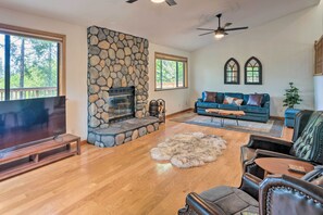 A spacious living room with a stone fireplace, a large flat-screen TV, leather furniture, and a view of the outdoors.