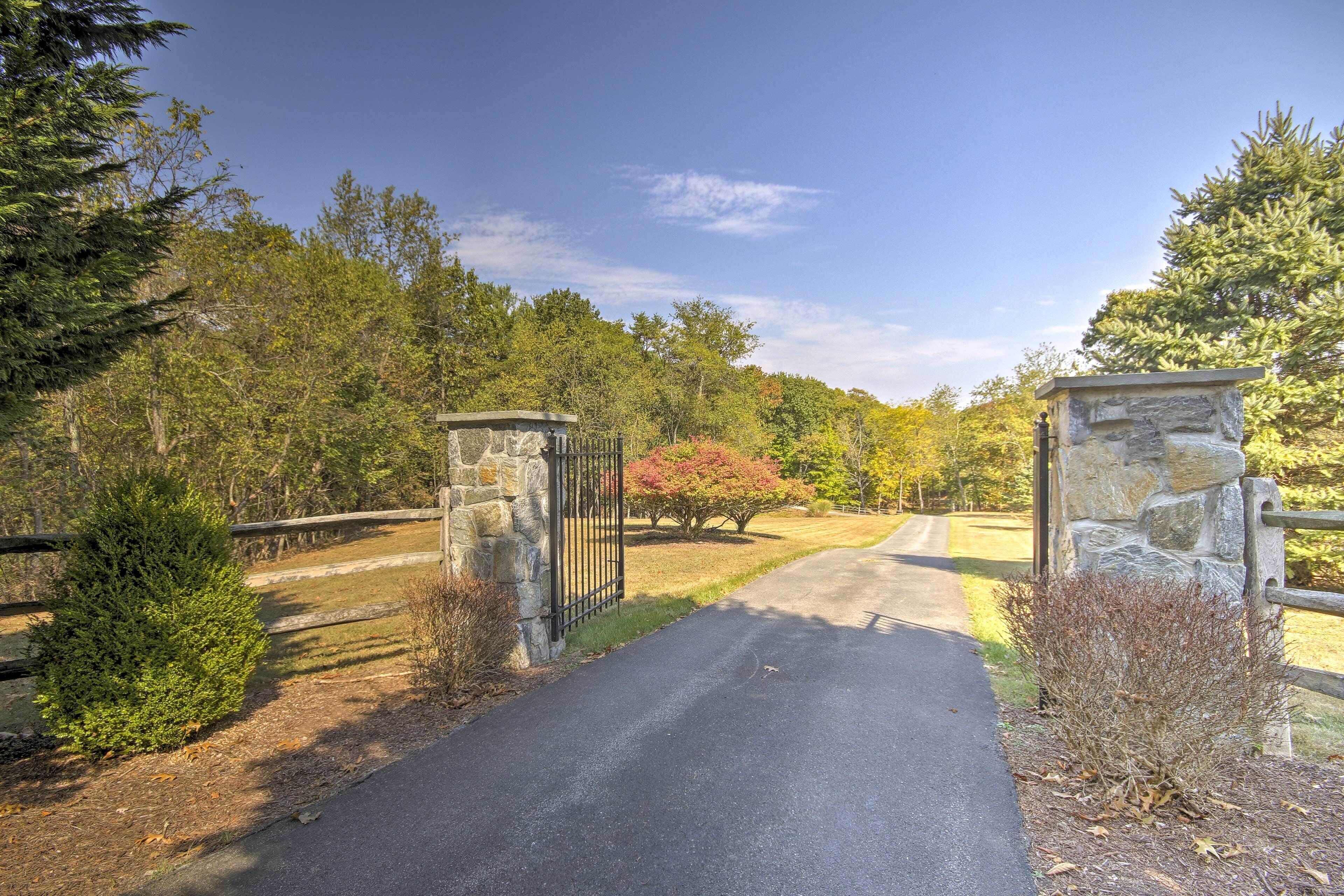 A paved driveway leading to a gated entrance with stone pillars and a metal gate.