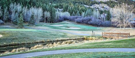 Un campo de golf con un puente de madera, un estanque y una casa al fondo.