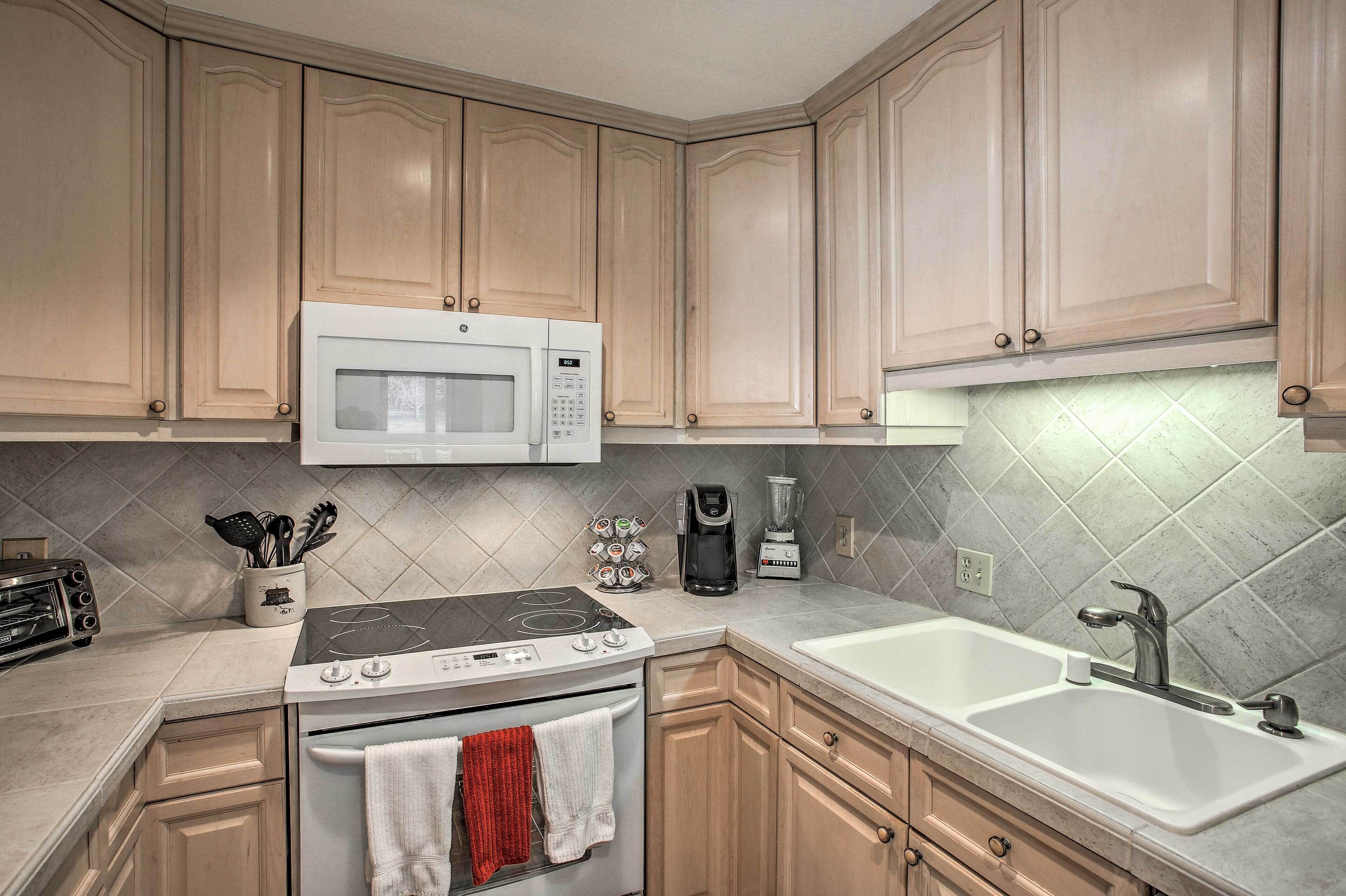 A kitchen with wooden cabinets, a microwave, a stove, a coffee maker, and a sink.