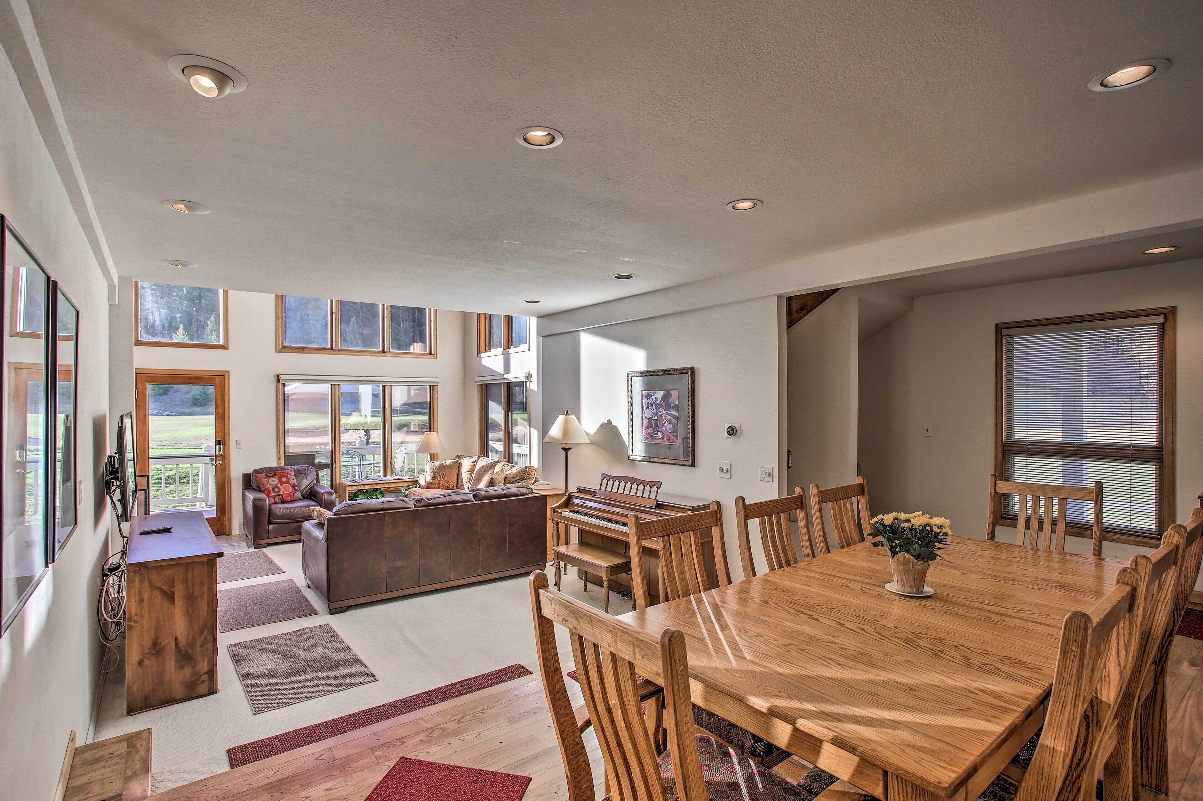 A spacious living room with a piano, a dining table, and a large window overlooking a scenic view.