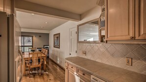 A kitchen with wooden cabinets, a tiled backsplash, and a dining area with a wooden table and chairs. - Colorado Home On Golf Course, Near Vail Ski Resort (Avon)