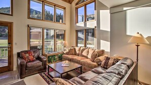 A spacious living room with a large sofa, a coffee table, and a leather armchair. There are multiple windows providing a view of the outdoors. - Colorado Home On Golf Course, Near Vail Ski Resort (Avon)