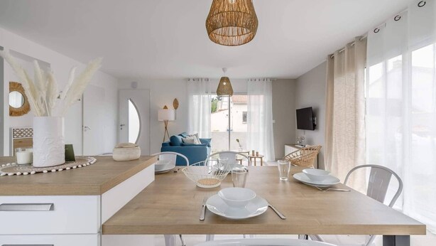 A modern dining area with a wooden table, white chairs, and a hanging light fixture. - Clair Jeanne - Climatisation - Plage (Notre-Dame-de-Monts)