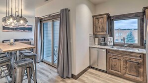 A modern kitchen with wooden cabinets, a built-in dishwasher, and a large window with a view of buildings. - Sleek Columbia Falls Condo: Centrally Located! (Columbia Falls)