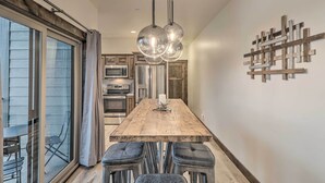 A modern kitchen with a wooden table, four bar stools, and a hanging light fixture. - Sleek Columbia Falls Condo: Centrally Located! (Columbia Falls)