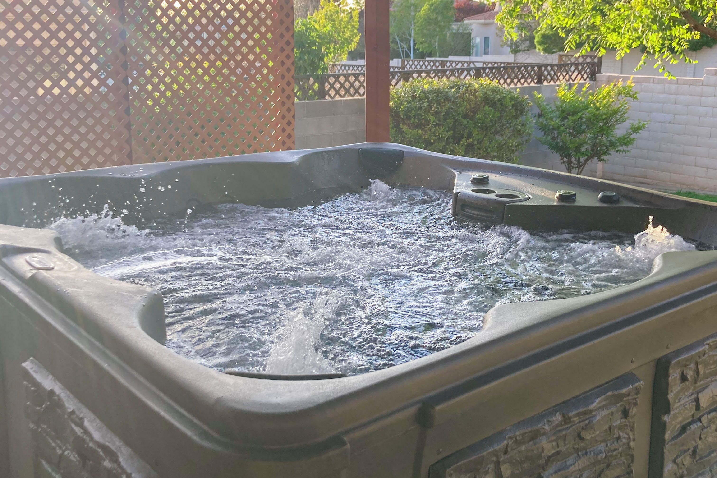A hot tub with water splashing, surrounded by a wooden fence and greenery.