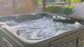 A hot tub with water splashing, surrounded by a wooden fence and greenery.