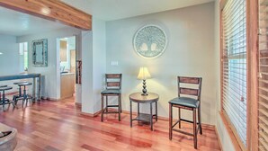 Una habitación amplia con pisos de madera, dos sillas de madera, una mesita redonda con una lámpara y un adorno de árbol montado en la pared.