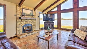 A spacious living room with a stone fireplace, a large TV, and a view of the water. - Lay Lake Access & Views: Expansive Shelby Home! (Shelby)