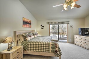 Quarto com cama, mesa de cabeceira, abajur, televisão, janela com vista e ventoinha no teto.