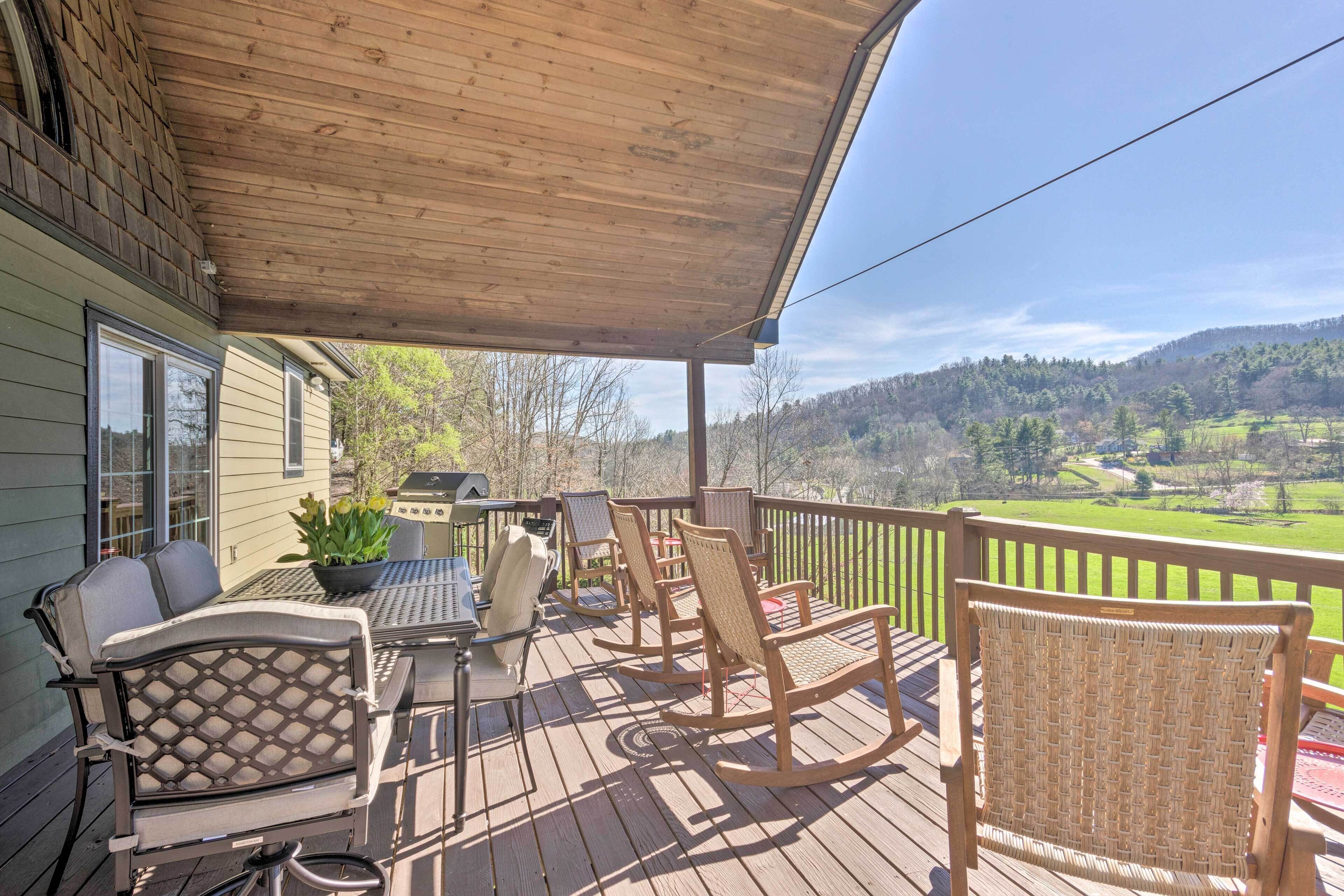 Une terrasse en bois, aménagée avec du mobilier d’extérieur, notamment des chaises et une table, qui offre une vue sur un paysage verdoyant.