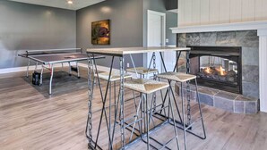 A room with a ping pong table, four bar stools, a fireplace, and a door. - Asheville Retreat w/ Game Room & Mountain Views! (Asheville)
