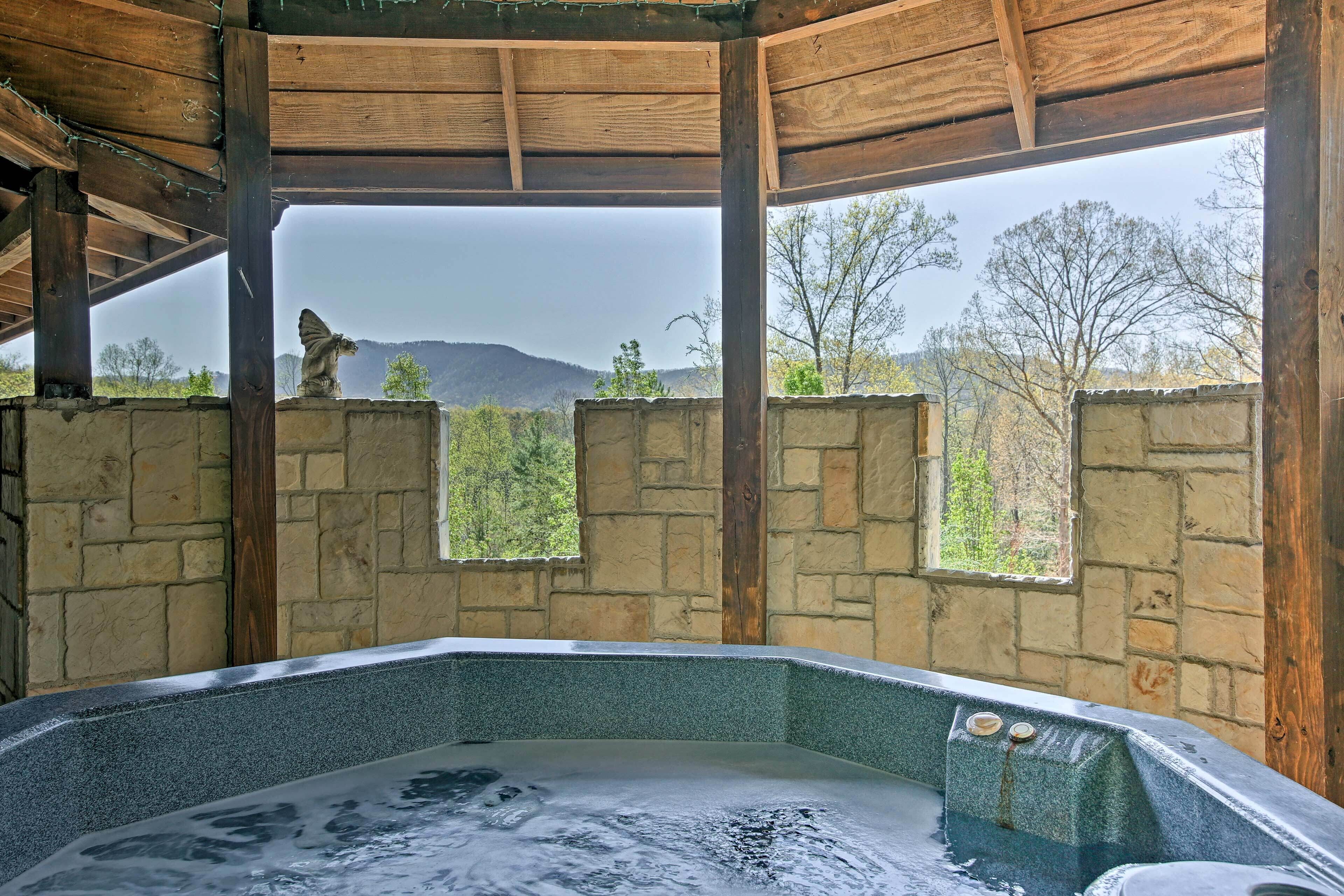A hot tub area with stone walls and wooden beams, a statue, and a view of trees and mountains.