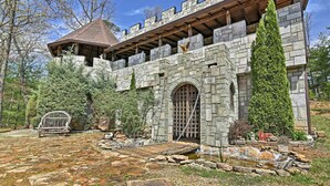 A stone building with a wooden balcony, a large arched entrance, and a small garden area with a swing set. - 11 Mi to Dtwn: Murphy Gem w/ Hot Tub & Mtn Views! (Murphy)