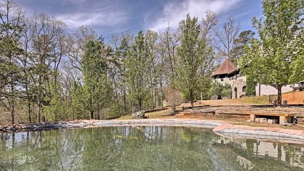 A serene outdoor area with a pond, trees, and a stone building with a thatched roof. - 11 Mi to Dtwn: Murphy Gem w/ Hot Tub & Mtn Views! (Murphy)