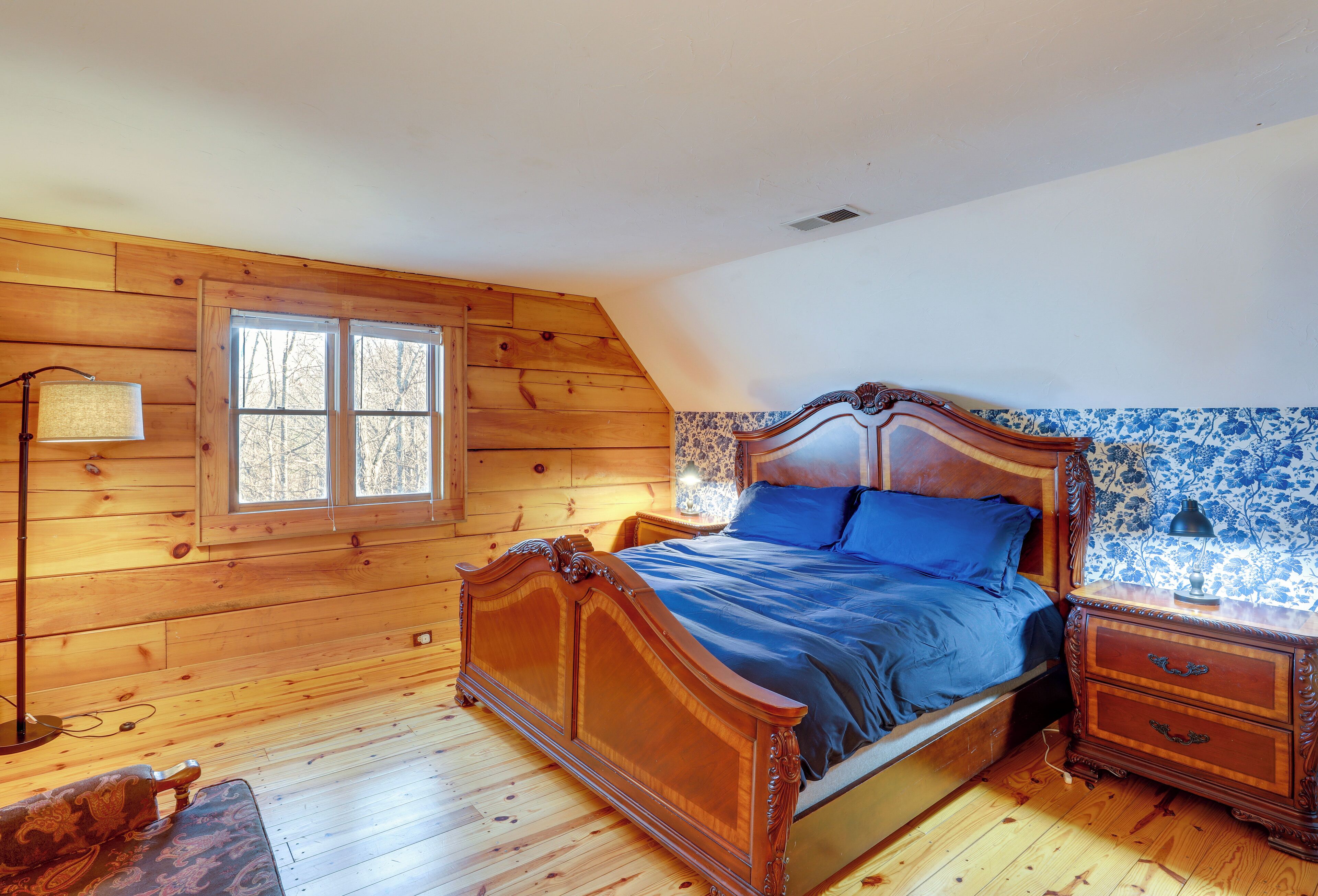 Een kamer met houten lambrisering, een bed, een nachtkastje en een lamp.