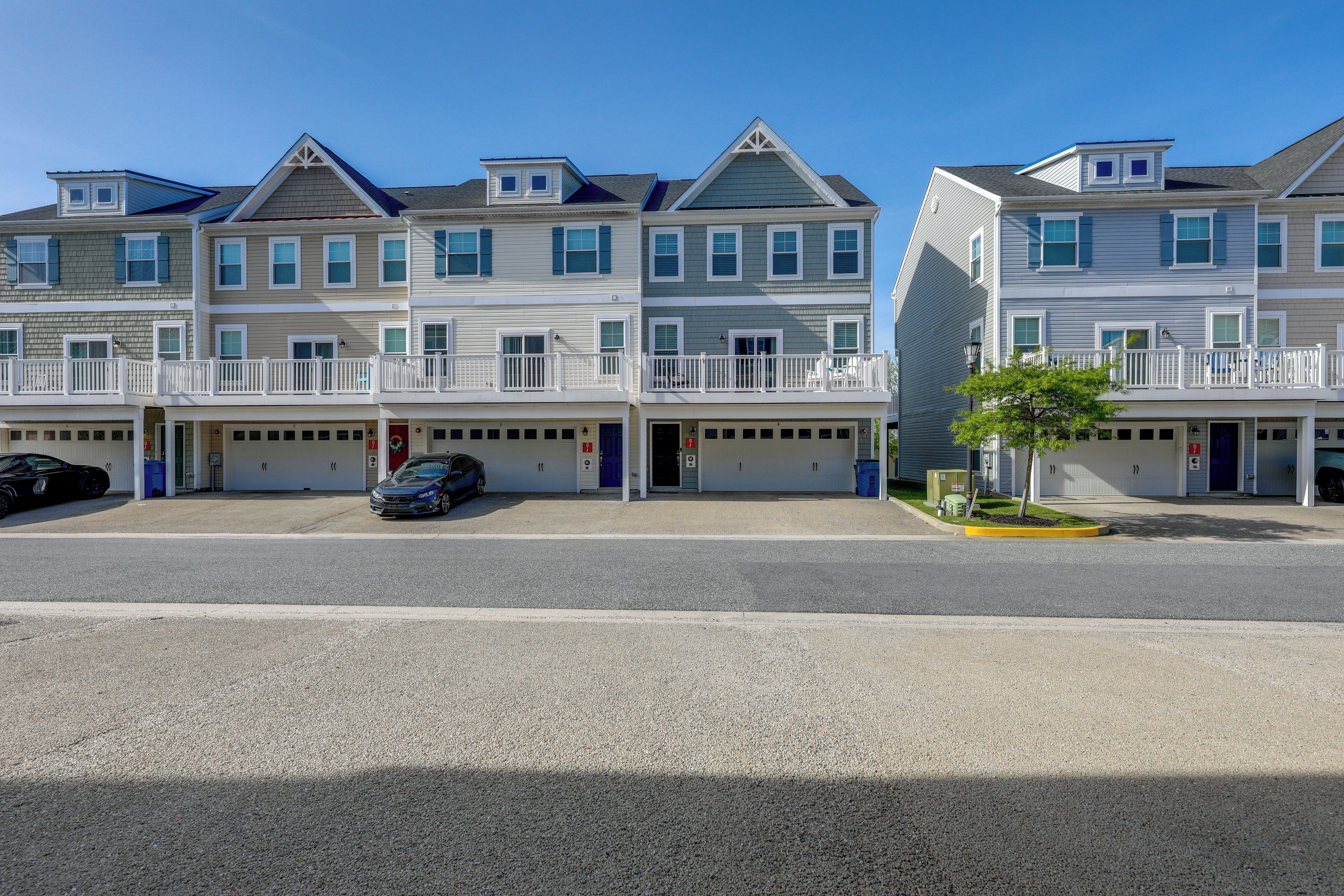 A row of townhouses with attached garages, a clear sky, and a tree in the foreground.