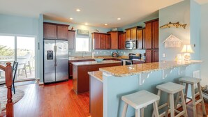A modern kitchen with wooden cabinets, a stainless steel refrigerator, granite countertops, and a large island with bar stools. - Boat Slip & Pool Access: Ocean City Home! (Ocean City)