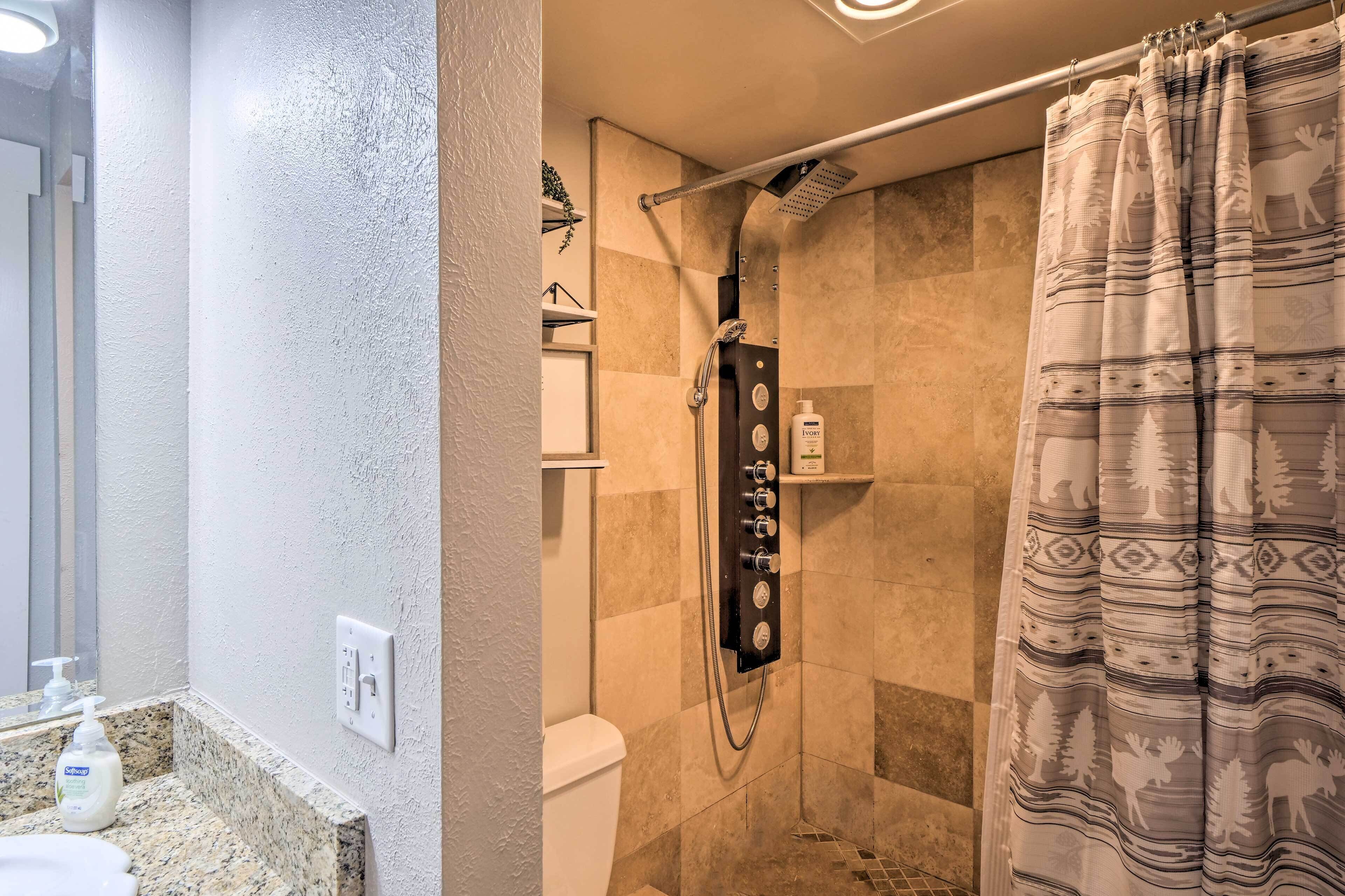 A bathroom with a shower, a toilet, a sink with a soap dispenser, and a towel rack.