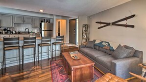 A modern kitchen with grey cabinets, a stainless steel refrigerator, and a dining area with a wooden table and chairs. - < 1 Mi to Peak 8: Ski Condo in Breck w/ Mtn Views (Breckenridge)