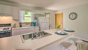 A modern kitchen with white cabinets, a stainless steel sink, a built-in oven, and a refrigerator. There are two bar stools and a clock on the wall. - Maggie Valley House w/ Mtn Views - 1 Mi to DT (Maggie Valley)