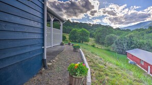 A house with a porch, a garden with potted plants, and a view of a green landscape with trees and a red building in the distance. - Maggie Valley House w/ Mtn Views - 1 Mi to DT (Maggie Valley)