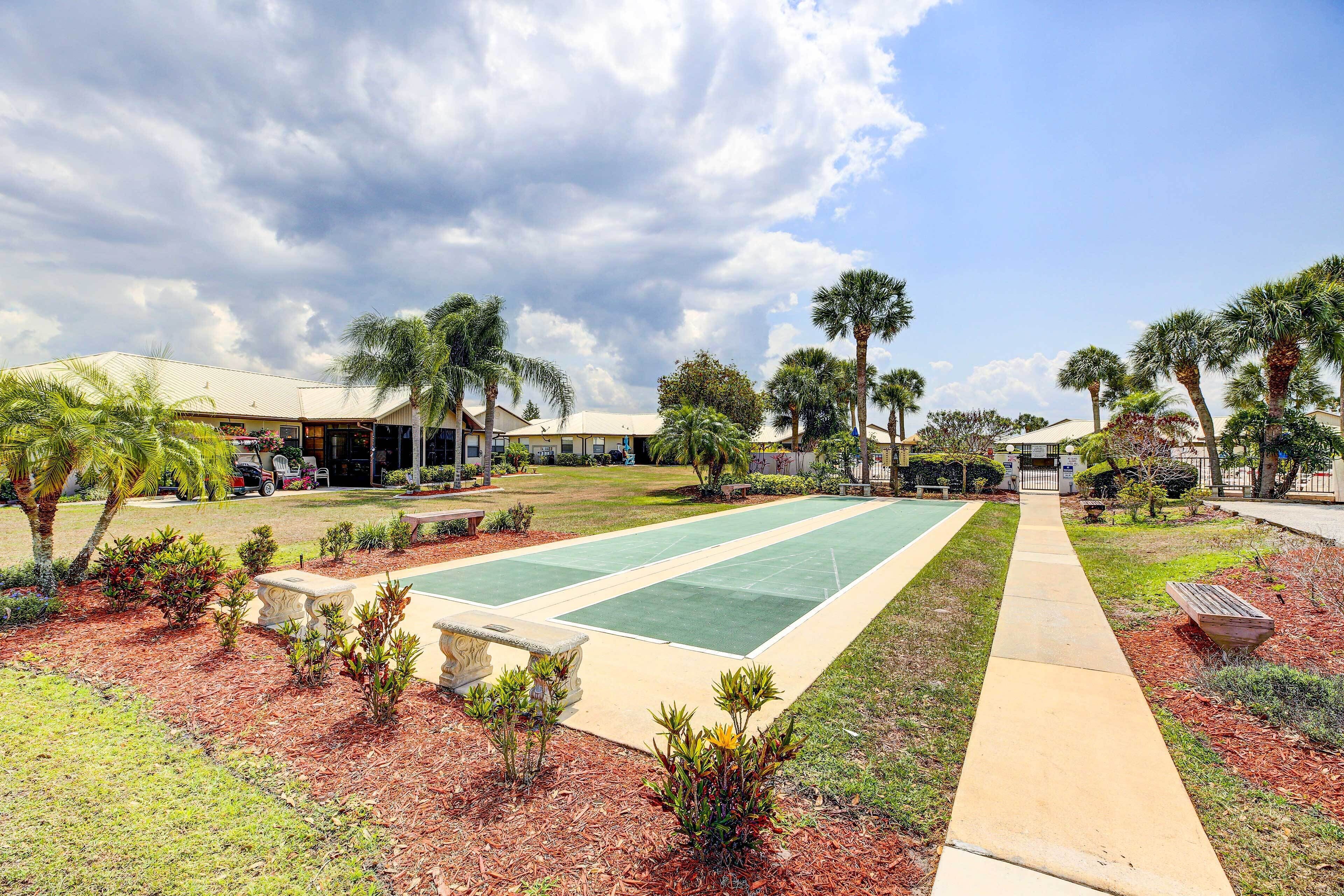 Una cancha de tenis con un jardín circundante, palmeras y un edificio de techo plano.